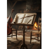 Ein hölzerner Notenständer mit Notenblättern, einem gerollten Pergament und einem Bleistift steht zwischen einem Cello und einem Blechblasinstrument in einem gemütlichen Raum mit einem Steinkamin und Holzstühlen.